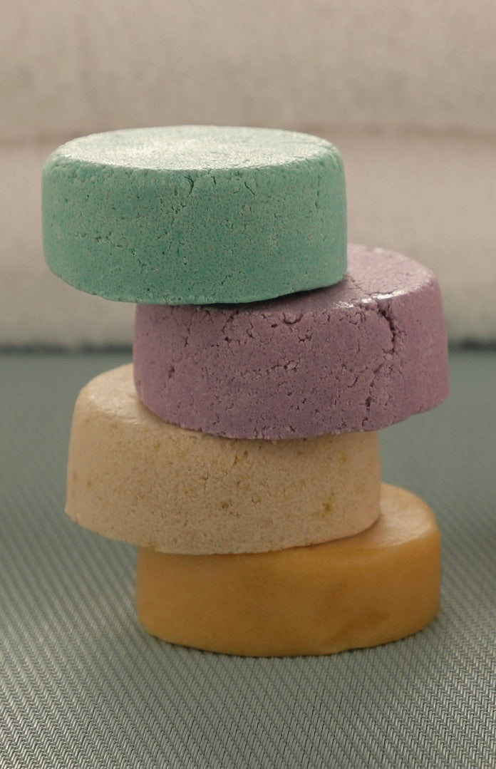 Stacked shampoo bars: teal-green, lavender-purple, and golden-yellow rounds