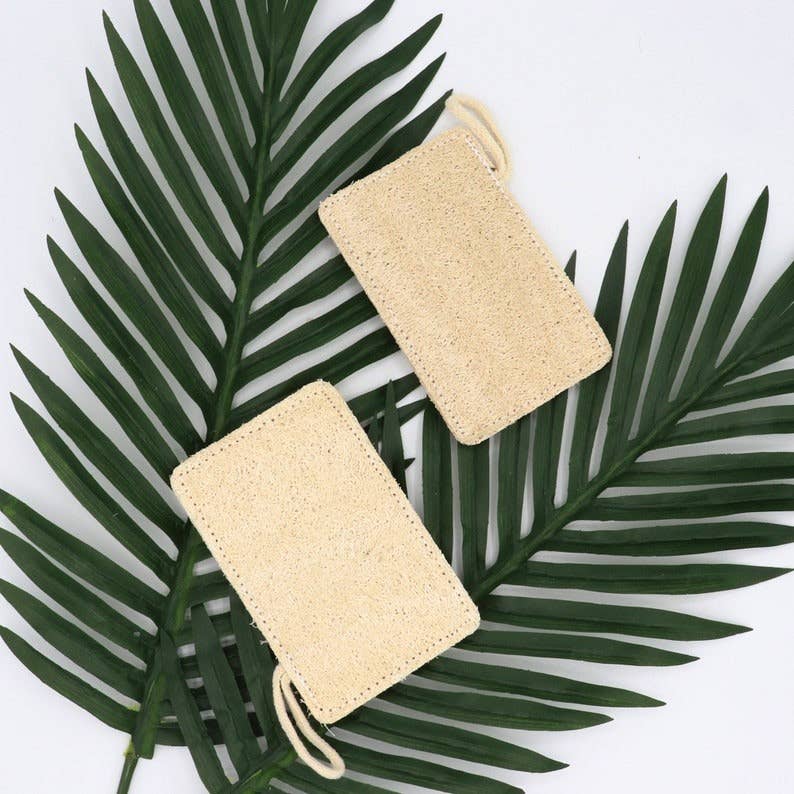 Two tan-beige loofah pads hanging with attached loop strings
