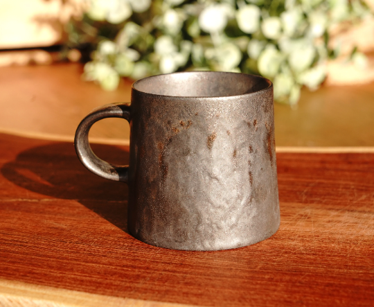 Stone-gray and bronze espresso mug on wooden table, speckled metal cup and handle