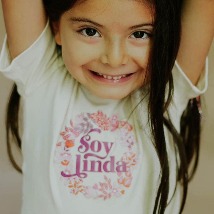 White tee on child with floral “Soy linda” logo print