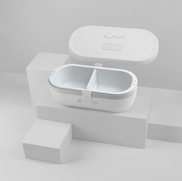 Closed white self-heating lunch box on a display base, with small front control icons.