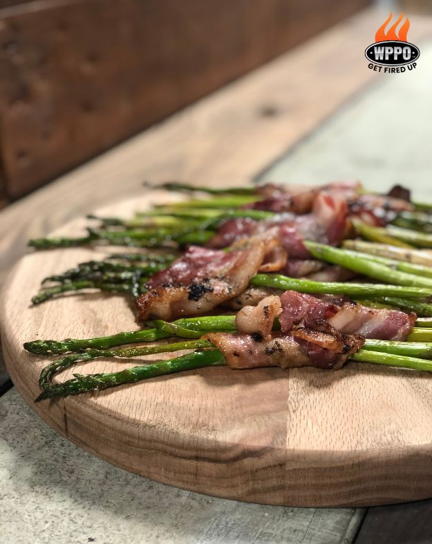 Grilled chicken and asparagus on round wooden board; WPP0 logo badge