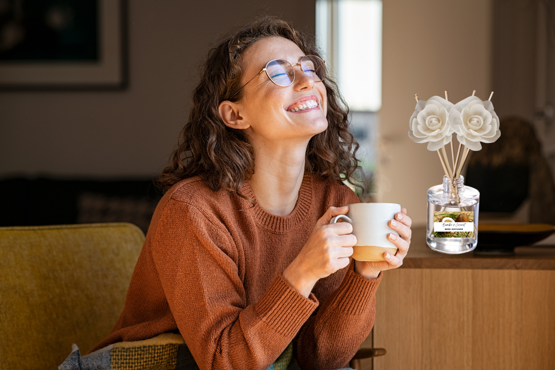 Clear reed diffuser with white rose-tipped reeds on table near a smiling woman