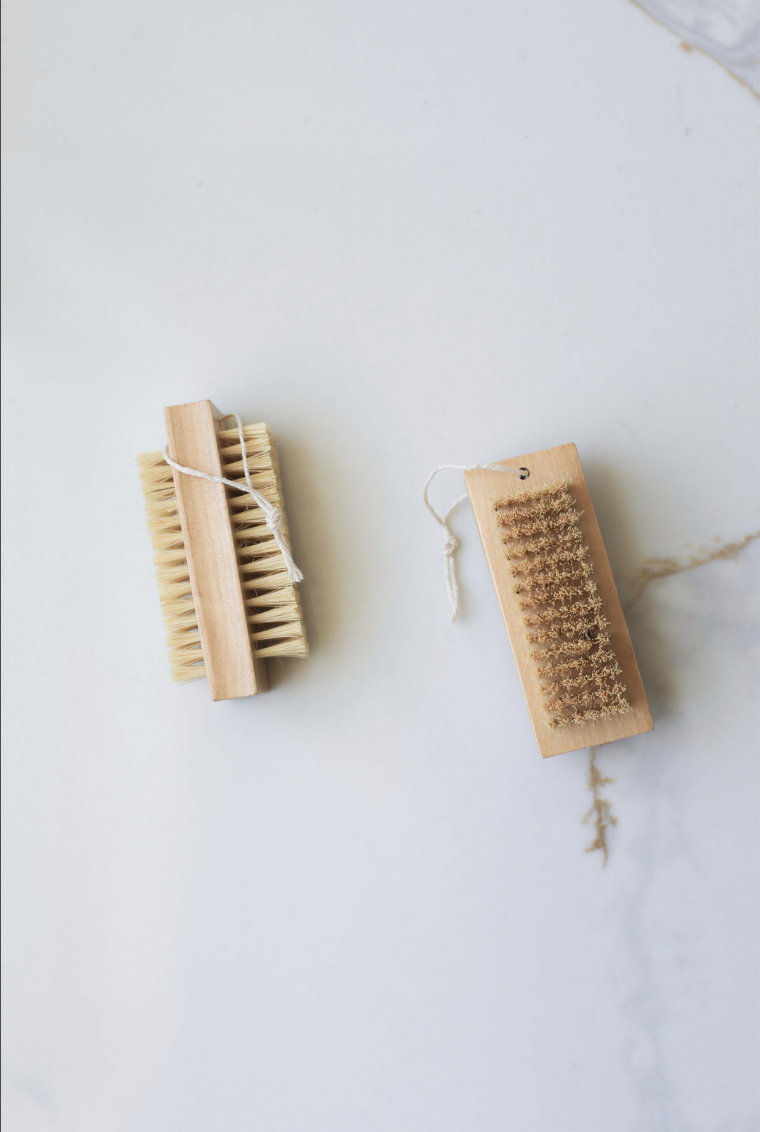 Double-sided nail brush with tan bristles on both sides and a paper tag