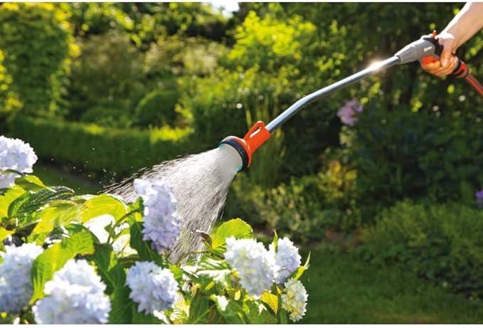 Orange trigger spray wand spraying water near blossoms with a wide spray head.
