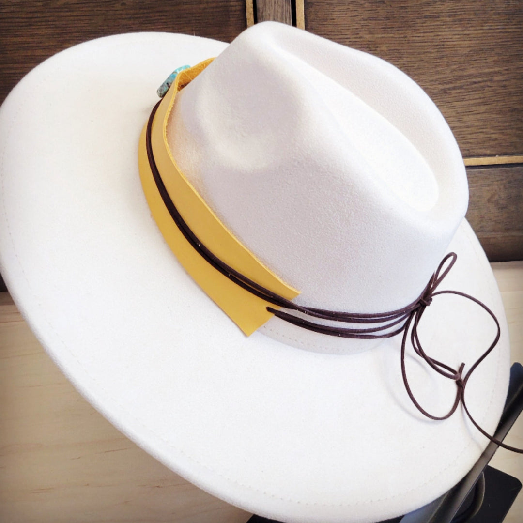 Wide-brim white felt hat with mustard leather band, turquoise buckle, and tied strings