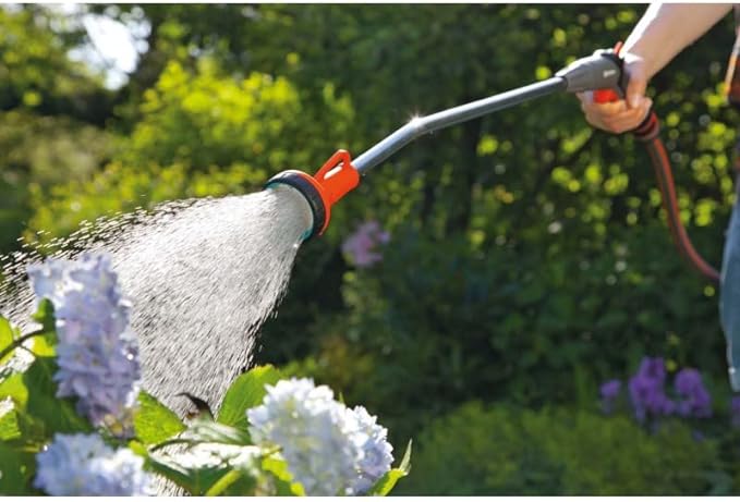 Orange-and-black trigger spray wand spraying water into a garden bed.