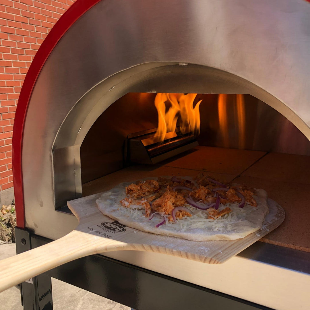 Wooden pizza peel lifting a topped pizza from an outdoor pizza oven