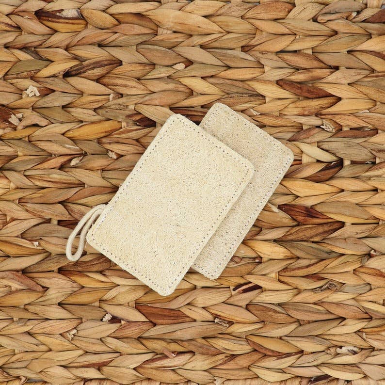 Two natural loofah pads with tied drawstring loop, textured tan-beige surface