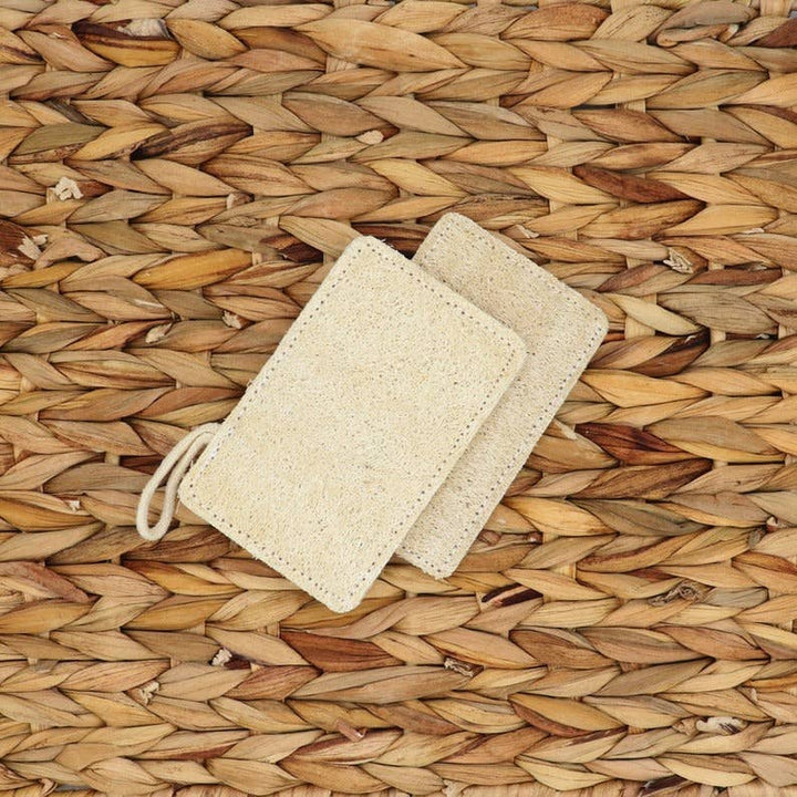 Two natural loofah pads with tied drawstring loop, textured tan-beige surface
