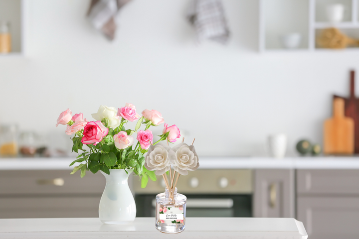 Clear glass reed diffuser with white rose-shaped reeds on a kitchen counter