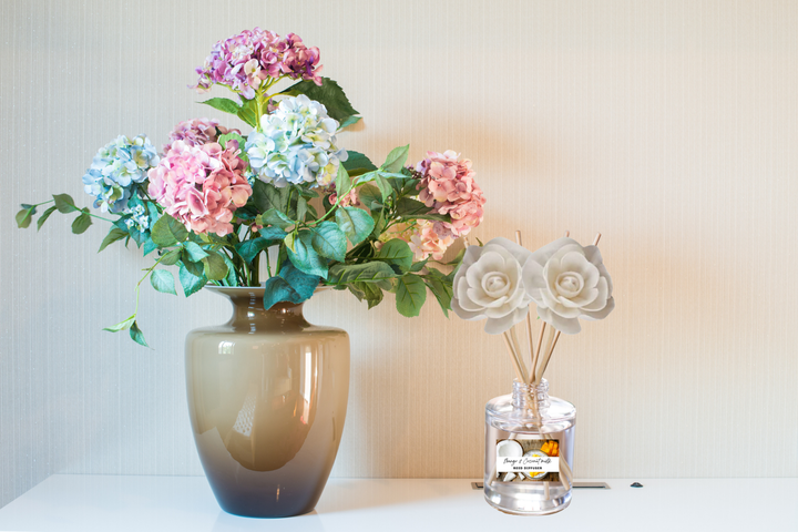Clear glass reed diffuser with multiple rose-shaped reeds and labeled bottle