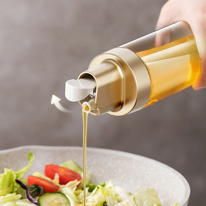 Clear glass oil dispenser with gold cap and spout pouring golden oil