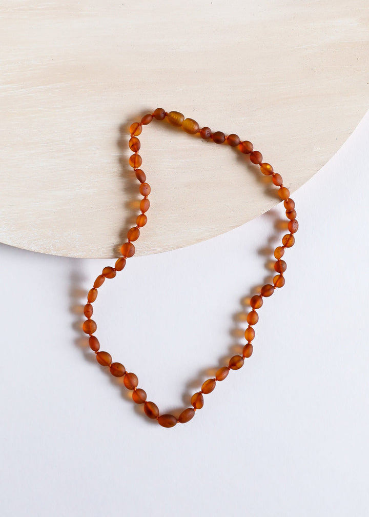 Cognac amber bead necklace with faceted oval beads shown on a light stone