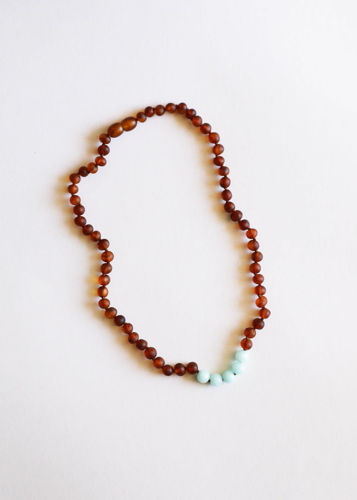 Raw amber bead necklace with turquoise stones at the lower curve