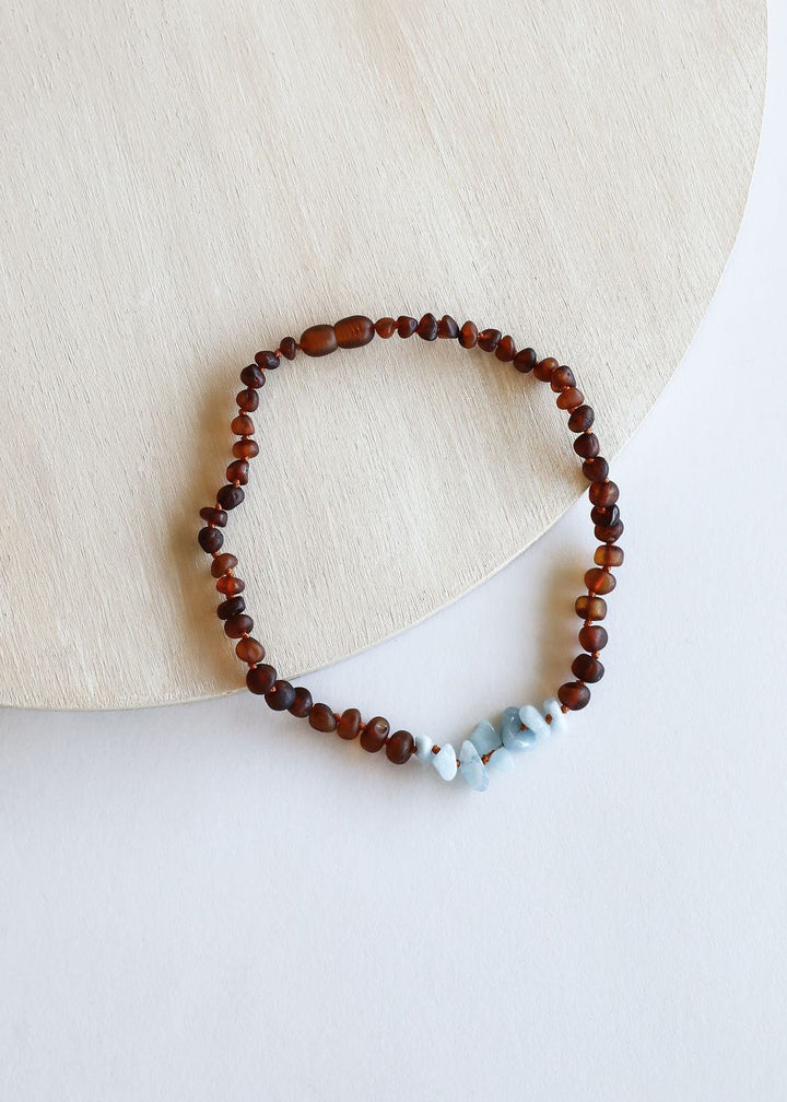 Amber brown bead necklace with light blue stone centerpiece detail, looped view