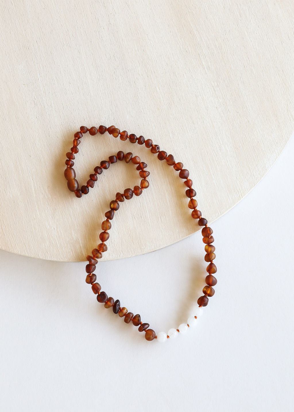Raw amber beaded necklace laid out flat with white moonstone bead details