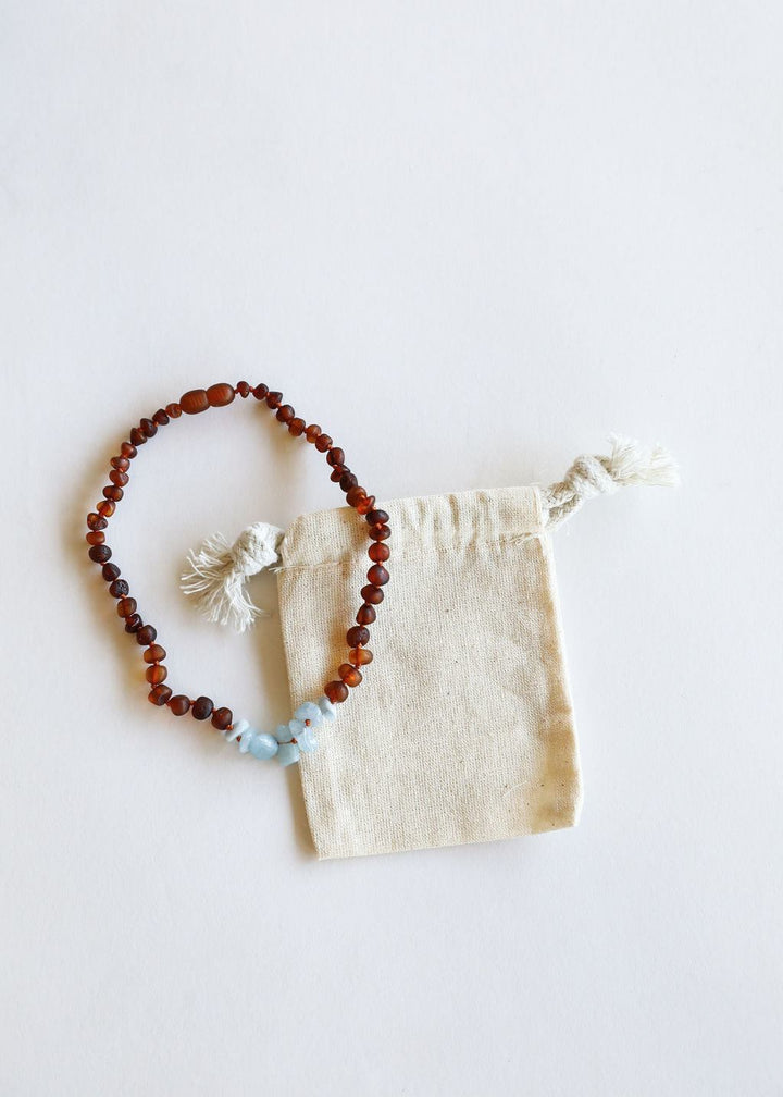 Amber brown bead necklace with light blue stone accents and small fabric pouch