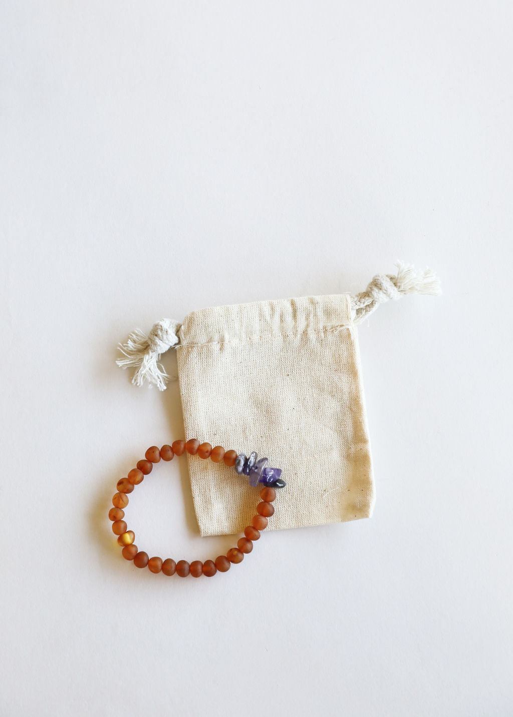 Amber-brown bead bracelet with purple amethyst laid on cream drawstring pouch