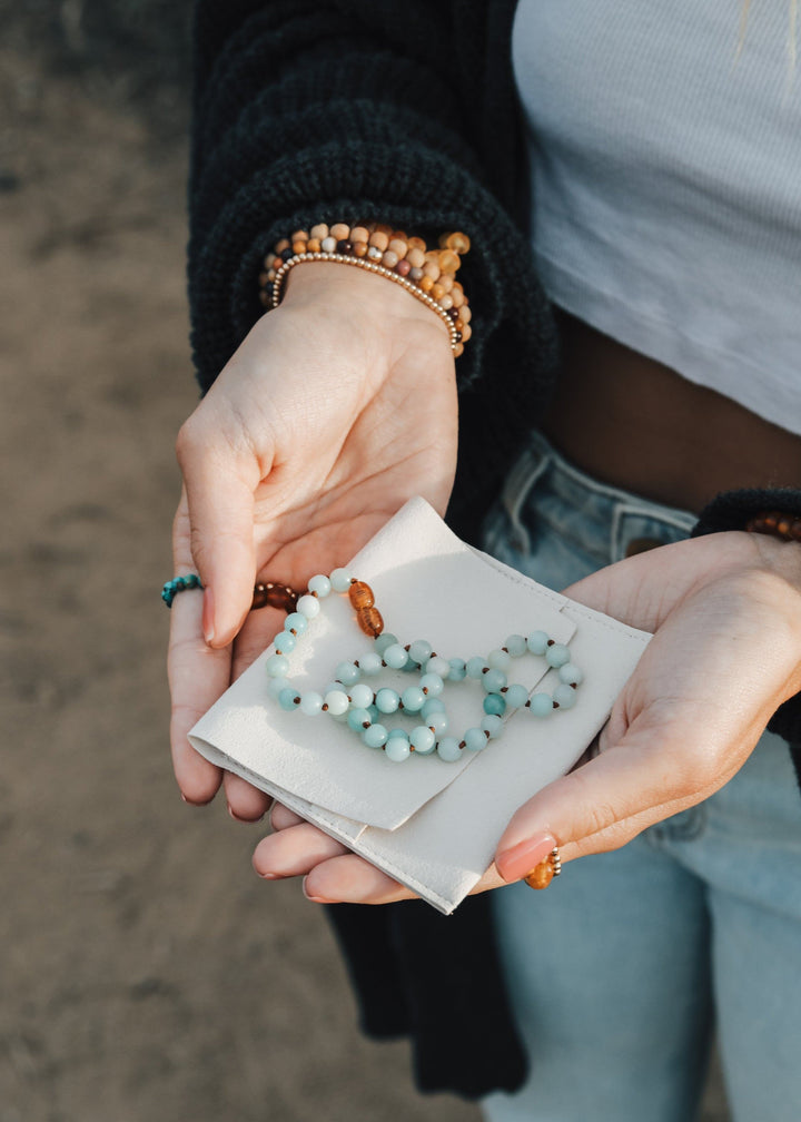 Amazonite beaded necklace held in hands, light blue beads with amber accent bead
