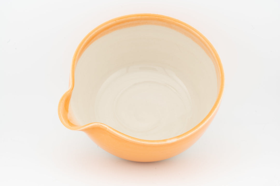 Orange ceramic bowl with side spout, cream interior