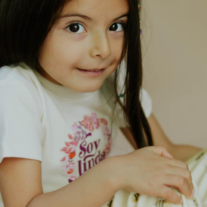 White crew-neck tee on child with floral “Soy linda” logo print
