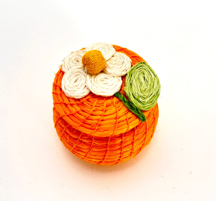 Orange round woven tiny basket with white, yellow, and green daisy-style flowers on top.