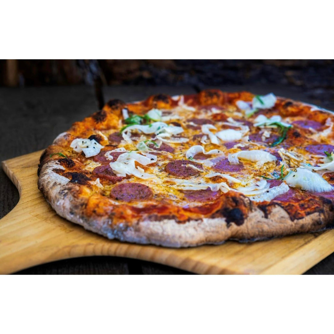 Wooden pizza peel holding a topped flat pizza on a wooden board