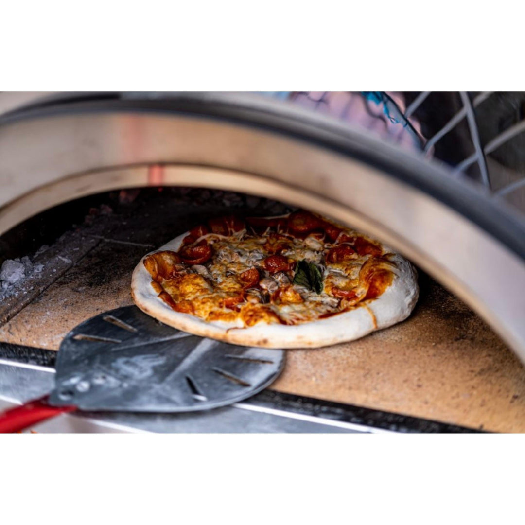 Round pizza peel sliding under a baked pizza inside a wood-fired oven