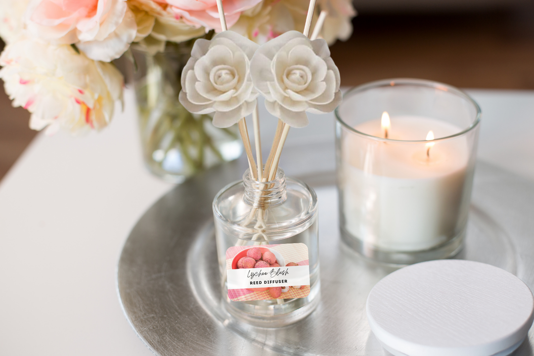Reed diffuser bottle with wooden reeds beside lit candle and rose decor