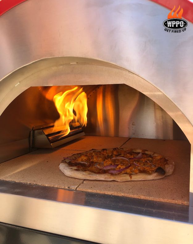 Pizza cooking inside the domed oven chamber with active flame