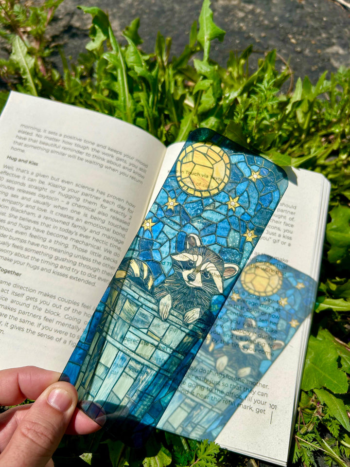 Raccoon-themed stained-glass style bookmark with blue city scene and moon