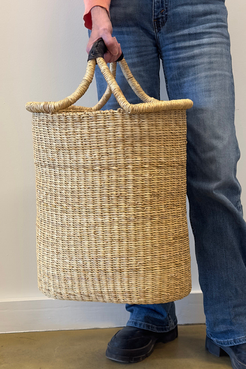 Woven pot basket with arched double handle loops, held at hip; natural tan weave