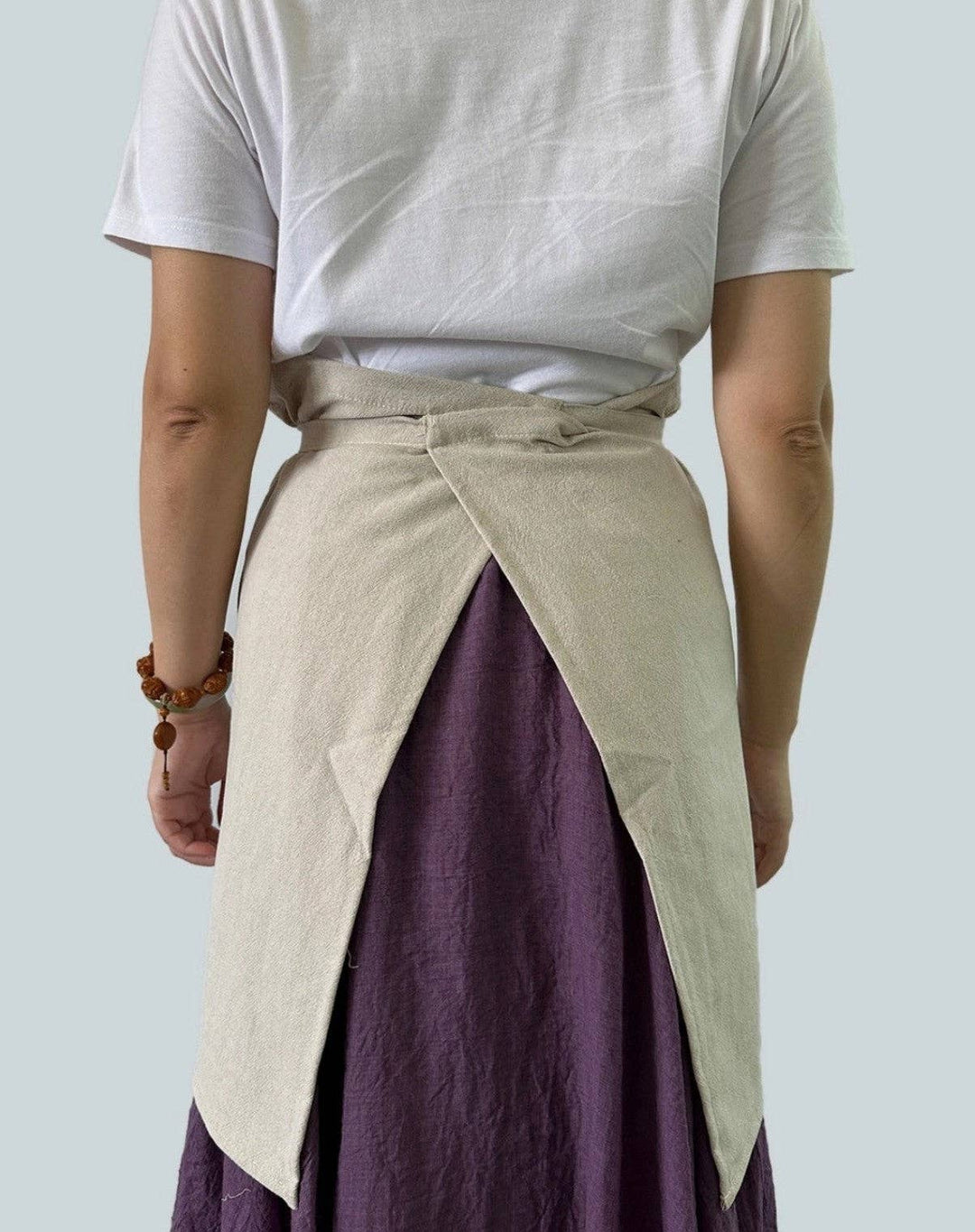 Light gray linen half apron with waist tie and diagonal front overlay over purple skirt