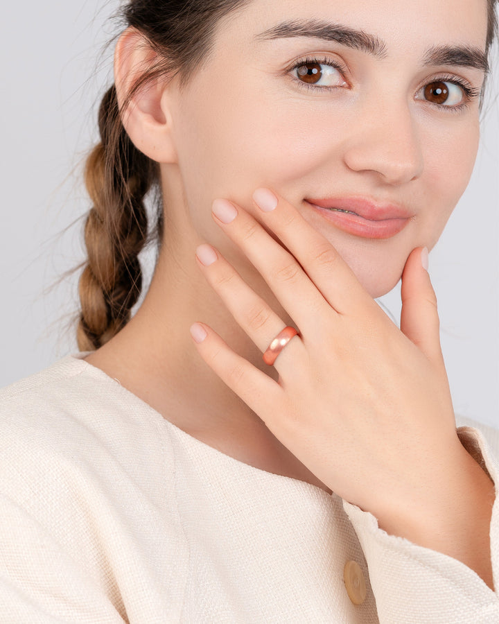 Copper domed ring on finger, hand resting near face with matching copper band visible