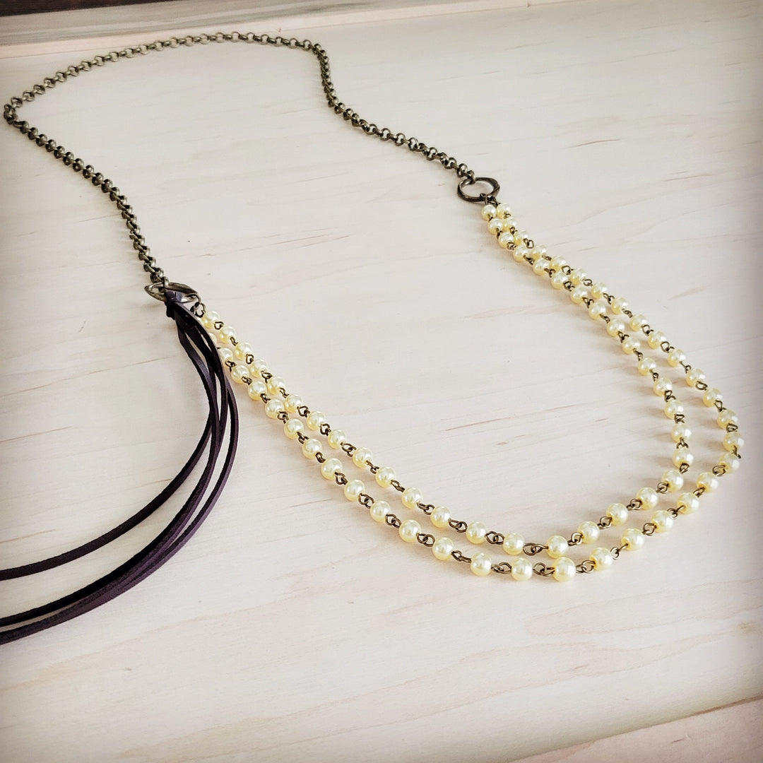 Double-strand champagne pearl necklace with black leather tassel ends and gold-tone links.