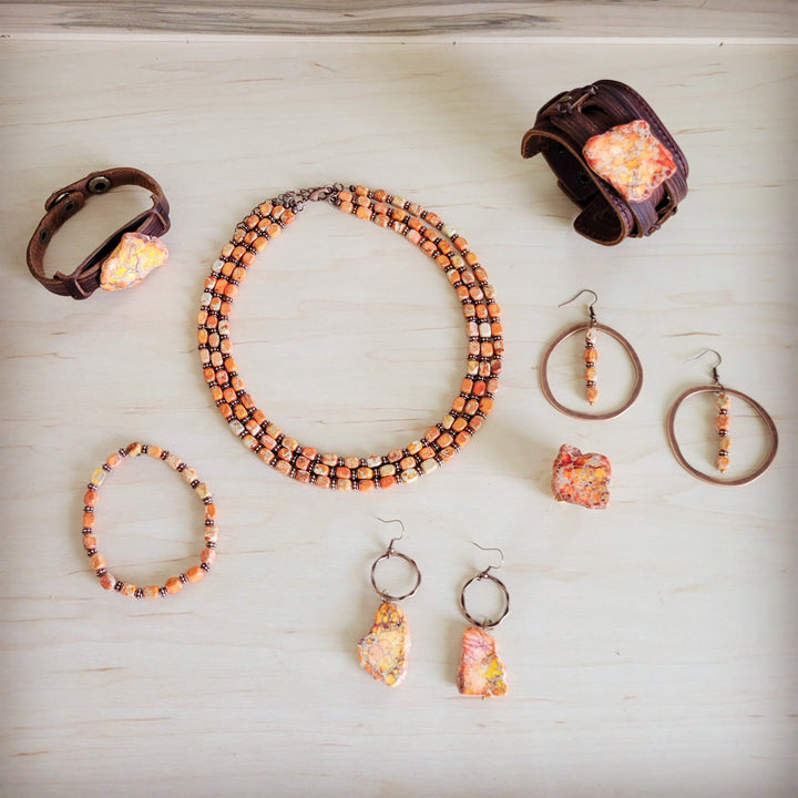 Copper hoop earrings with orange bead dangles, shown with matching pieces.