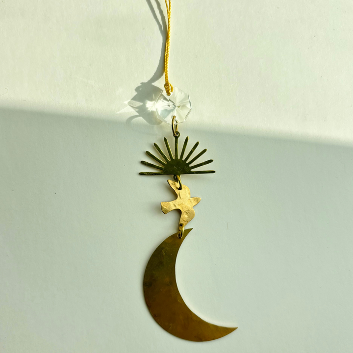 Gold crescent moon ornament with winged figure and starburst detail, hanging on ribbon