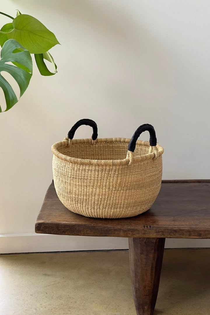 Natural woven basket with two black handles, rounded open top