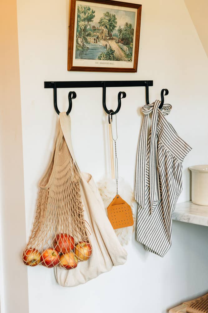 Wrought iron wall rack with three hooks holding bags and towels