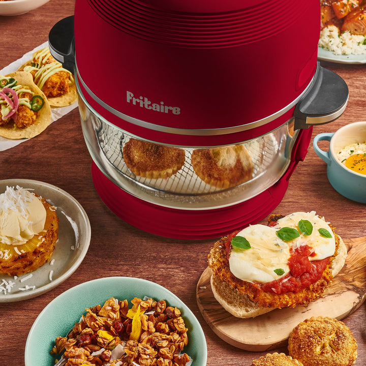 Red air fryer with open glass chamber, surrounded by plated cooked meals.
