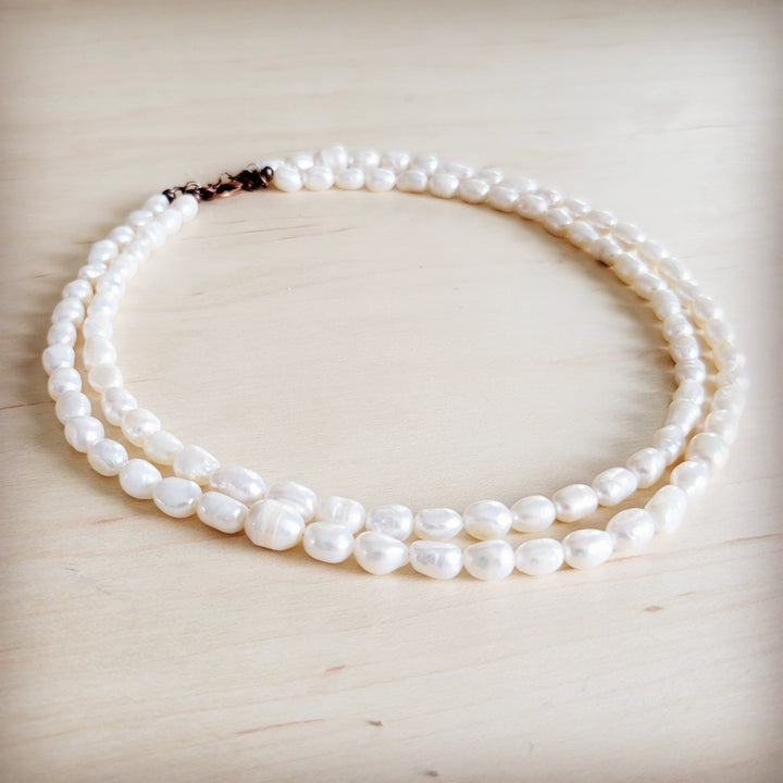 Double-strand freshwater pearl necklace resting flat, rose-tone clasp at one end