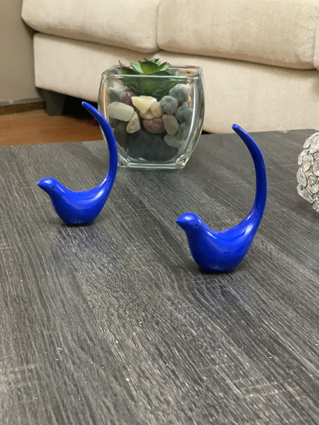 Blue bird figurine pair with glass jar and decorative stones on a tabletop