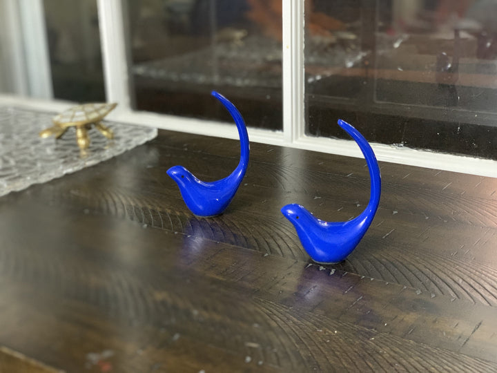 Blue bird figurine pair on dark wood floor near a window