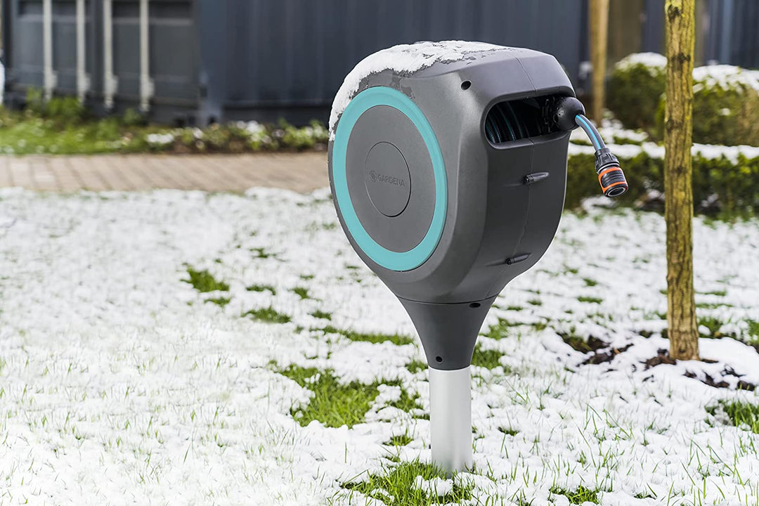 Roll-up garden hose reel with blue ring outdoors on snow-dusted grass