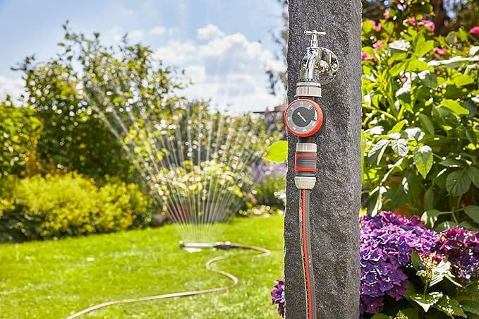 Garden hose timer with orange flow dial mounted on post, watering spray