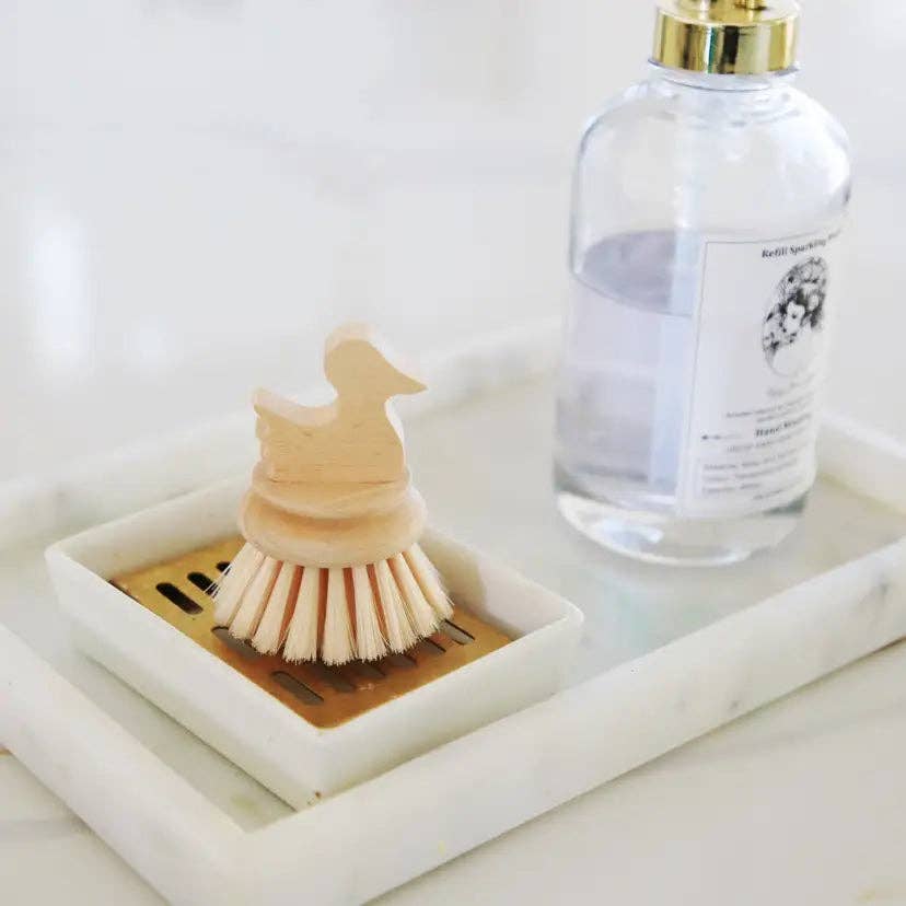 Bird-shaped wooden kids cleaning brush with white bristles on square dish