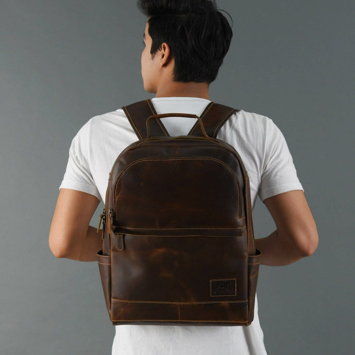 Brown buffalo leather backpack worn by model; padded straps and back panel with logo patch.