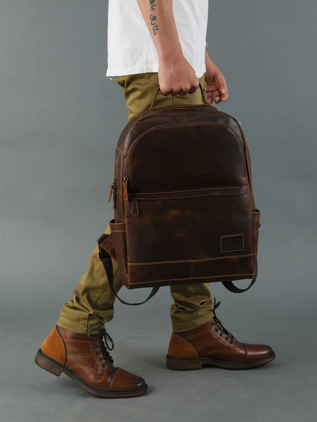 Brown buffalo leather backpack carried at side; adjustable strap and front zipper pocket.