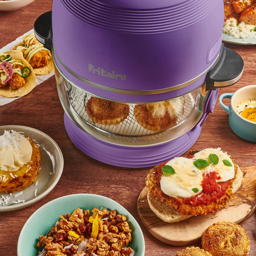Purple lavender air fryer with clear glass chamber, surrounded by plated meals
